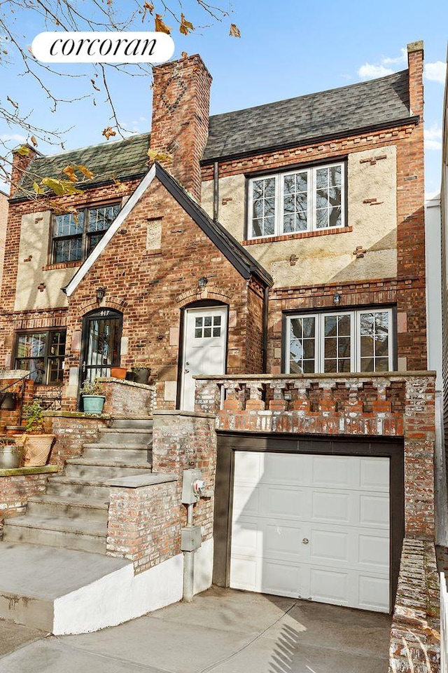 english style home featuring brick siding, a chimney, concrete driveway, and an attached garage