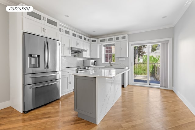 kitchen with a sink, stainless steel appliances, under cabinet range hood, white cabinetry, and light wood-type flooring