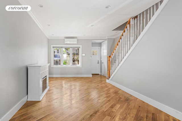 unfurnished living room with stairway, light wood finished floors, a wall mounted air conditioner, and ornamental molding