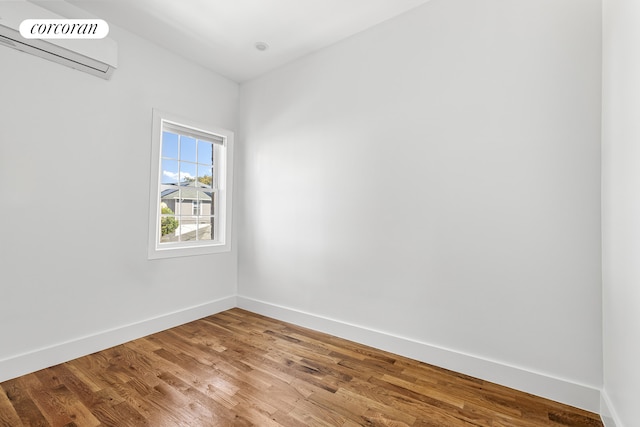 unfurnished room with wood finished floors, baseboards, and a wall mounted air conditioner