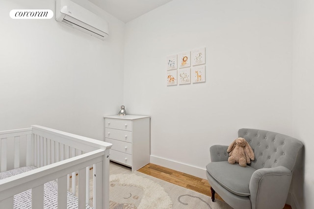 bedroom with a wall mounted air conditioner, a crib, light wood-style floors, and a wainscoted wall