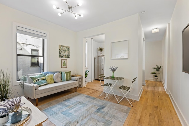 living room with an inviting chandelier, light wood-style floors, and baseboards