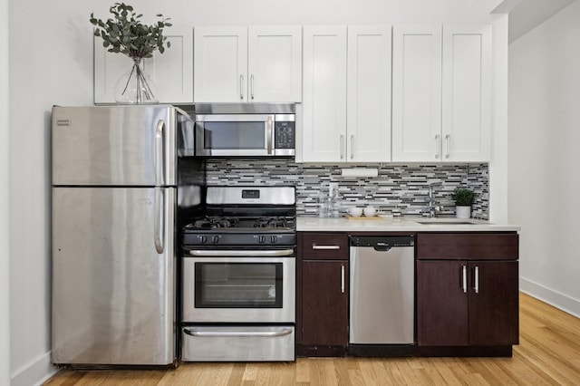 kitchen featuring decorative backsplash, appliances with stainless steel finishes, light countertops, light wood-style floors, and white cabinetry