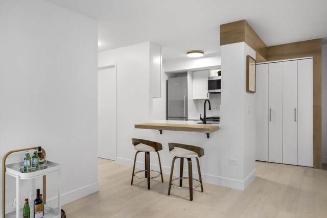 kitchen with a peninsula, a breakfast bar, white cabinetry, and light wood-style floors