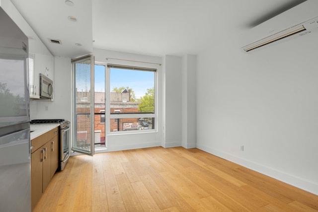 kitchen featuring stainless steel appliances, a wall unit AC, and light hardwood / wood-style floors