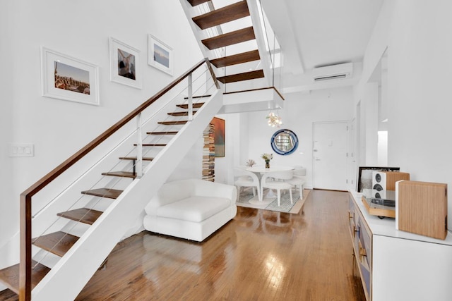 staircase with a chandelier, hardwood / wood-style floors, a high ceiling, and an AC wall unit