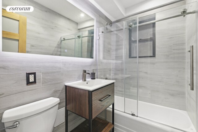 full bath featuring visible vents, toilet, shower / bath combination with glass door, vanity, and tile walls