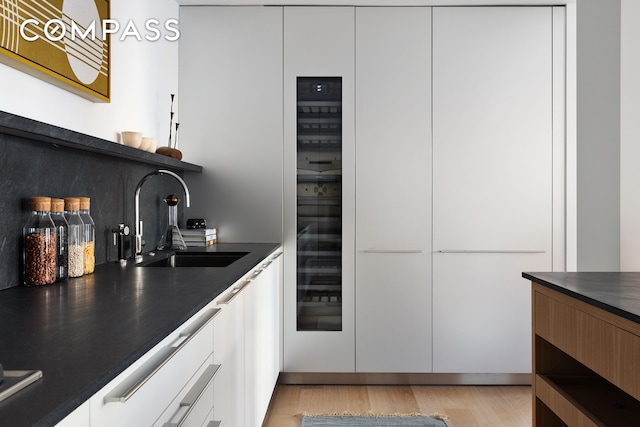 kitchen featuring dark countertops, light wood finished floors, a sink, white cabinetry, and modern cabinets