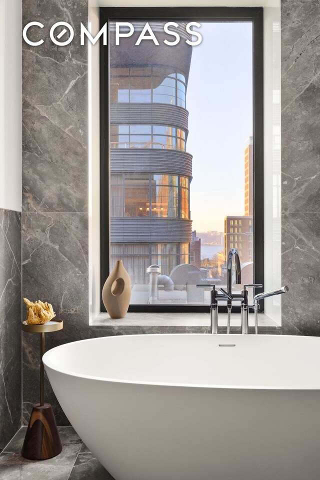 full bath with a city view, marble finish floor, tile walls, and a freestanding tub