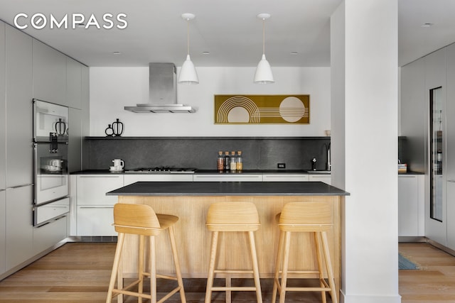 kitchen with dark countertops, wall chimney range hood, and light wood-type flooring