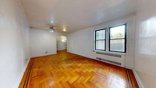 unfurnished room with ceiling fan, light parquet flooring, and radiator heating unit