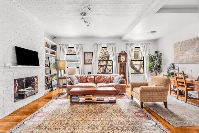 living room with built in features, a brick fireplace, a textured ceiling, and wood finished floors