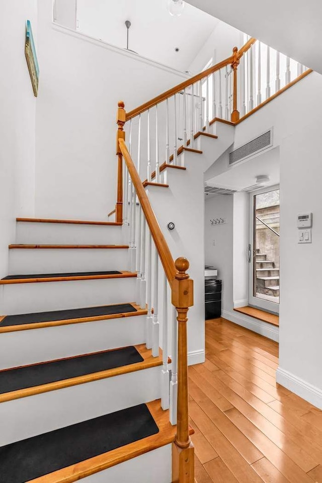 staircase with visible vents, baseboards, high vaulted ceiling, and wood finished floors