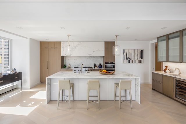 kitchen with beverage cooler, oven, a kitchen island with sink, and hanging light fixtures