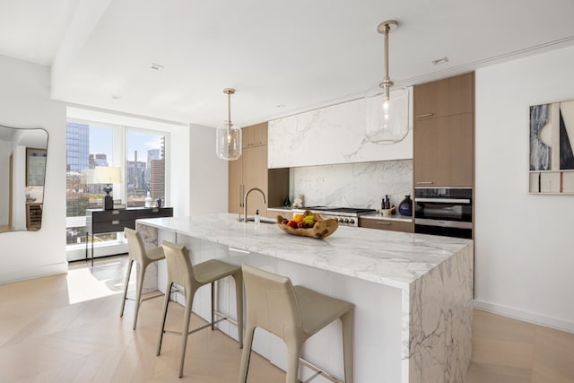 kitchen with pendant lighting, appliances with stainless steel finishes, backsplash, light stone countertops, and a center island with sink