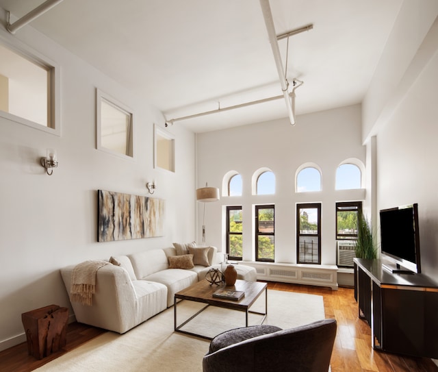 living room featuring a towering ceiling, rail lighting, and light wood-style flooring