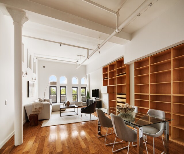 dining space with built in shelves, hardwood / wood-style flooring, decorative columns, and a high ceiling