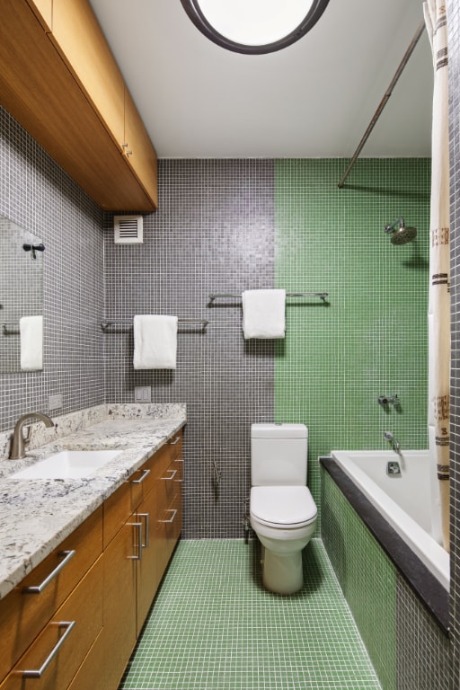 full bath featuring toilet, tile patterned floors, tiled shower / bath combo, vanity, and tile walls