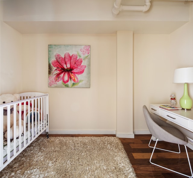 bedroom featuring a nursery area, dark wood-style flooring, and baseboards