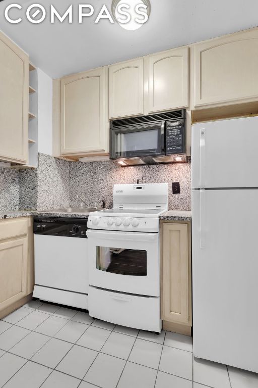 kitchen with light tile patterned floors, backsplash, light brown cabinets, and white appliances