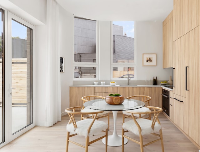 kitchen featuring breakfast area, light brown cabinets, sink, light wood-type flooring, and oven