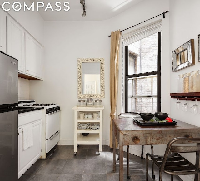 kitchen featuring backsplash, white range with gas stovetop, white cabinets, and stainless steel refrigerator