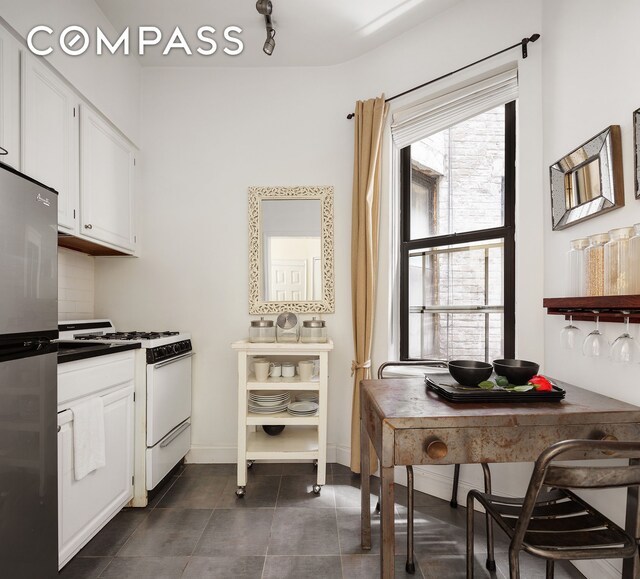 330 E 90th St Unit 3D, New York City, NY 10128 - kitchen with white gas range, dark countertops, freestanding refrigerator, and white cabinets