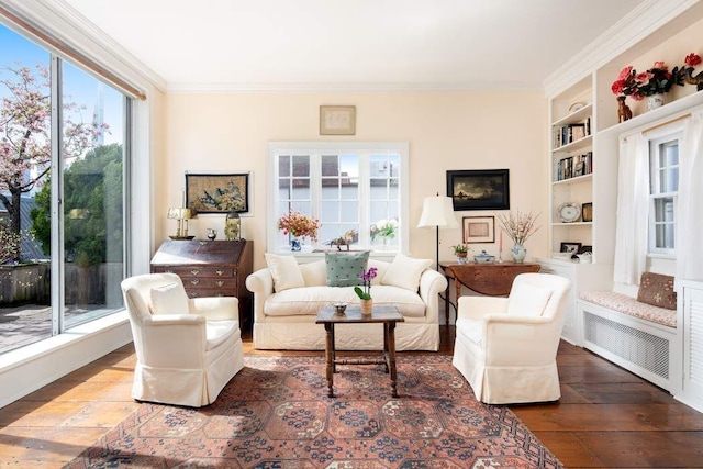 sitting room with wood-type flooring, ornamental molding, and built in shelves