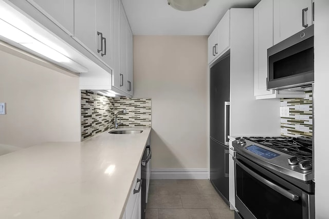 kitchen featuring tile patterned flooring, stainless steel appliances, a sink, white cabinetry, and light countertops