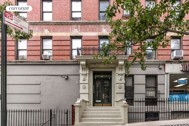 doorway to property featuring fence, cooling unit, and brick siding