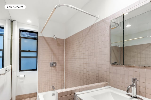 bathroom featuring tiled shower / bath, tile walls, and sink