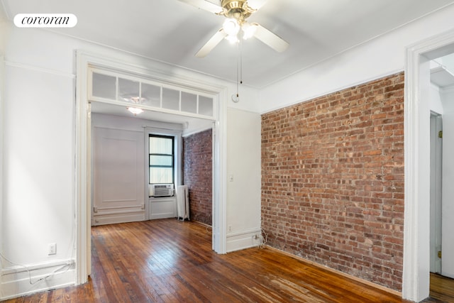 empty room with brick wall, radiator heating unit, cooling unit, ceiling fan, and dark wood-type flooring