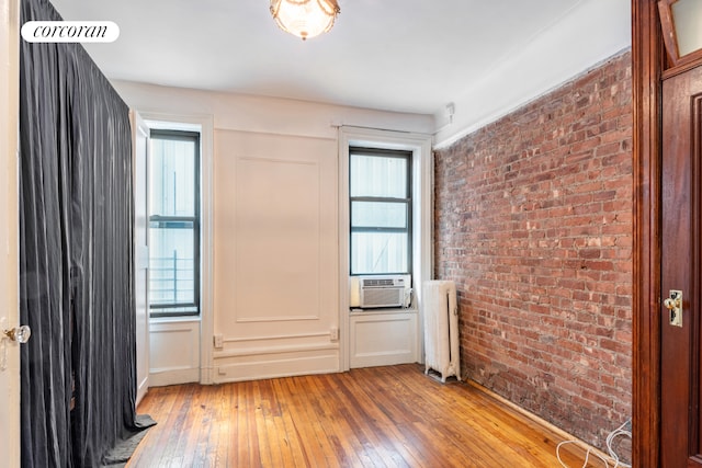 interior space with radiator heating unit, a healthy amount of sunlight, light wood-type flooring, and brick wall