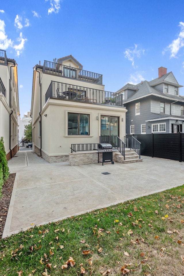 rear view of house with a patio, a balcony, fence, and stucco siding