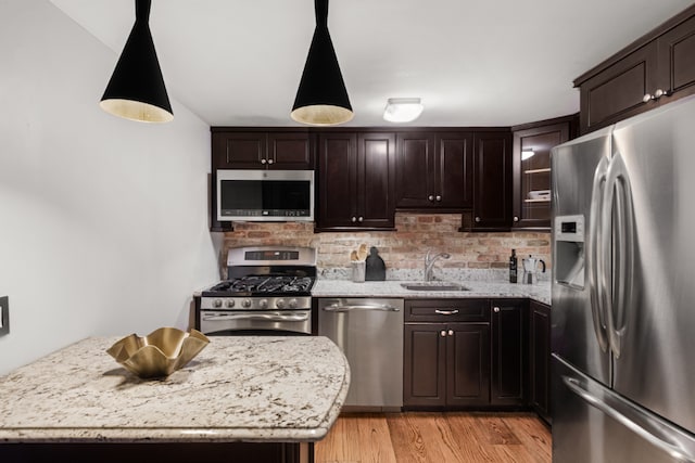 kitchen with dark brown cabinetry, sink, light stone counters, pendant lighting, and stainless steel appliances