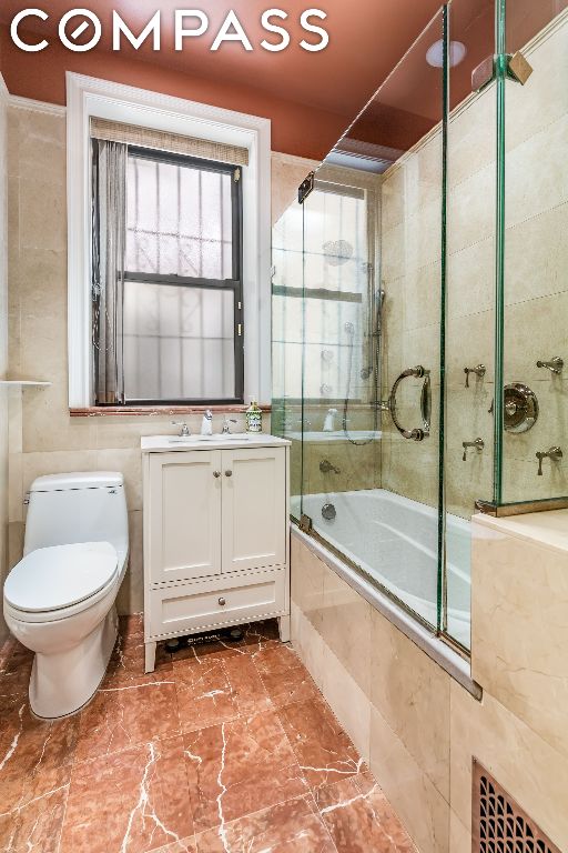 full bathroom with toilet, tile walls, vanity, and shower / bath combination with glass door