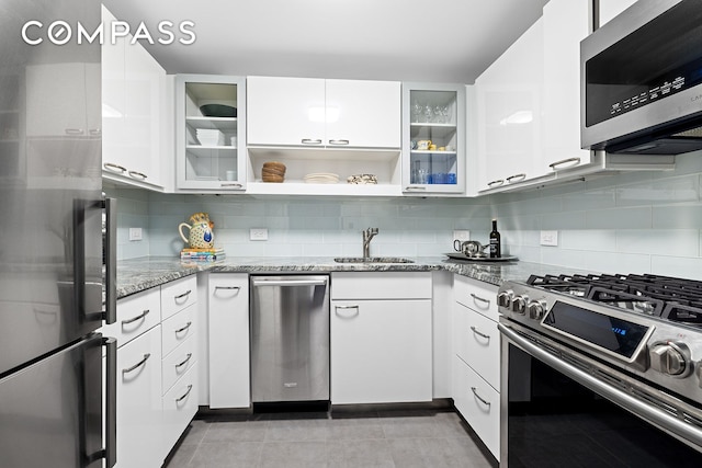 kitchen featuring appliances with stainless steel finishes, a sink, tasteful backsplash, white cabinets, and light stone countertops
