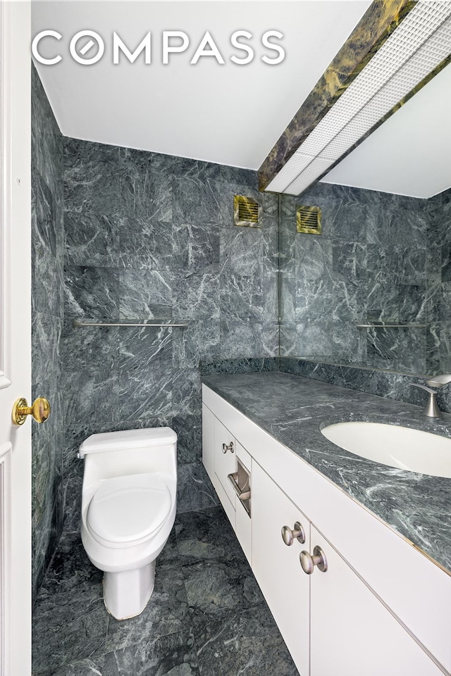 bathroom featuring vanity, tile walls, and toilet