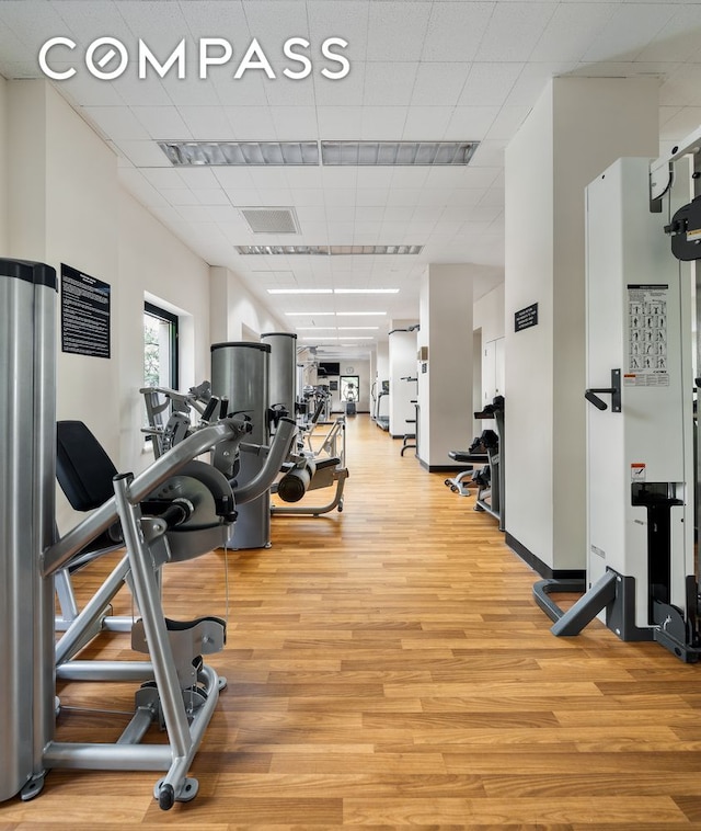 exercise room with a drop ceiling and light wood-type flooring