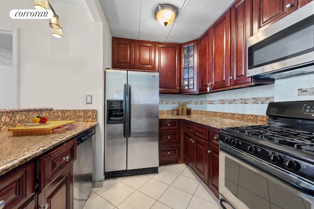 kitchen featuring light stone counters, decorative light fixtures, light tile patterned floors, appliances with stainless steel finishes, and decorative backsplash