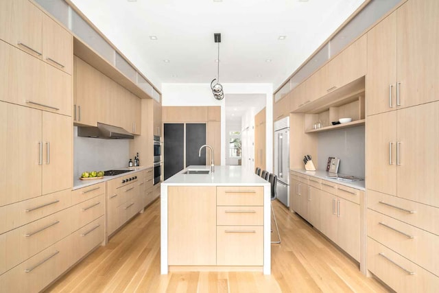 kitchen with light countertops, light brown cabinetry, appliances with stainless steel finishes, a sink, and an island with sink