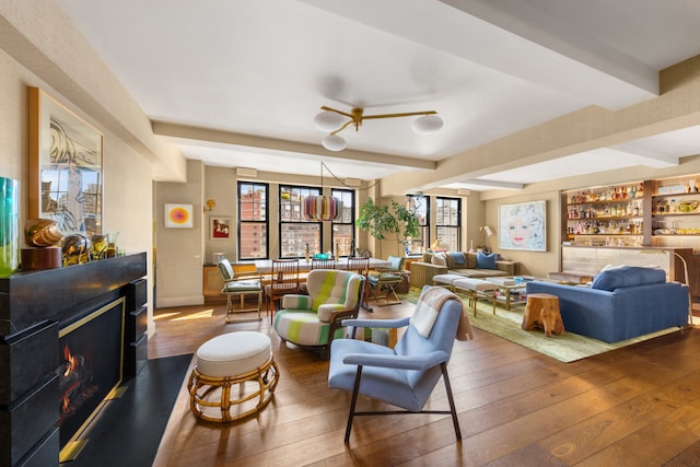 living room with a warm lit fireplace, beam ceiling, a healthy amount of sunlight, and dark wood finished floors