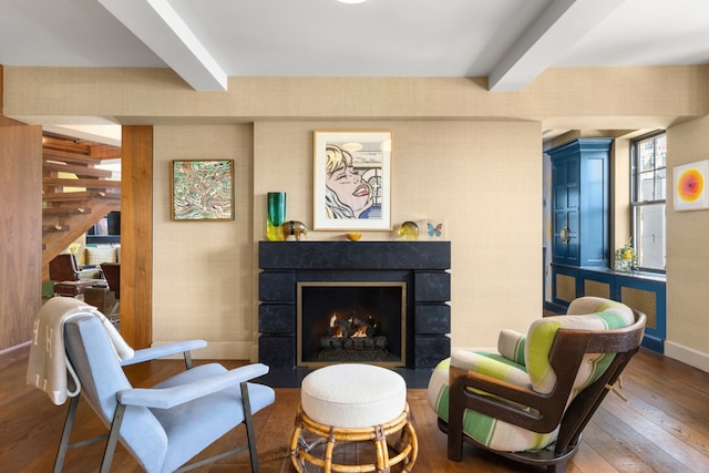 living area featuring beam ceiling, hardwood / wood-style floors, a fireplace with flush hearth, baseboards, and stairs