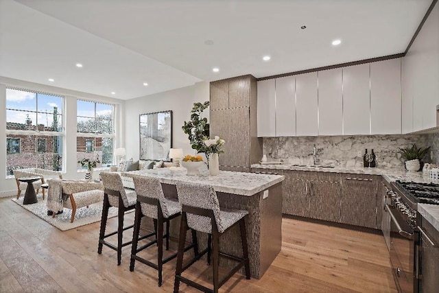 kitchen with light stone countertops, high end range, a kitchen island, sink, and backsplash