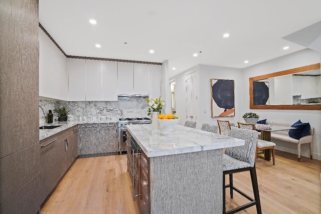 kitchen featuring a kitchen island, stainless steel stove, a breakfast bar area, white cabinets, and light stone counters