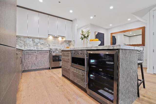 kitchen with white cabinetry, decorative backsplash, a kitchen breakfast bar, wine cooler, and high end range