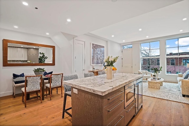 kitchen with light hardwood / wood-style floors, a kitchen breakfast bar, stainless steel microwave, and a kitchen island