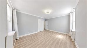 spare room with baseboards, crown molding, and light wood finished floors