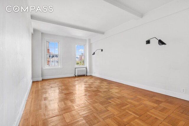 empty room with radiator heating unit, baseboards, and beam ceiling