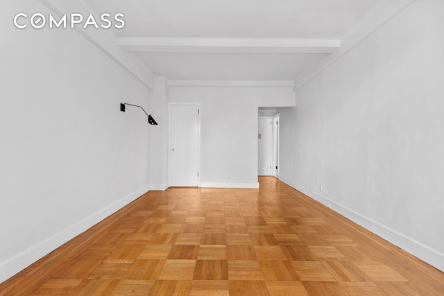 empty room featuring beamed ceiling and baseboards